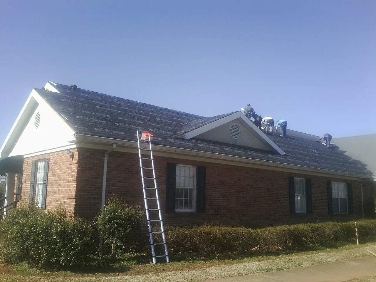 Crew tearing shingles off a brick ranch roof with a ladder set — Emergency Roof Repair work by our crew in Industry