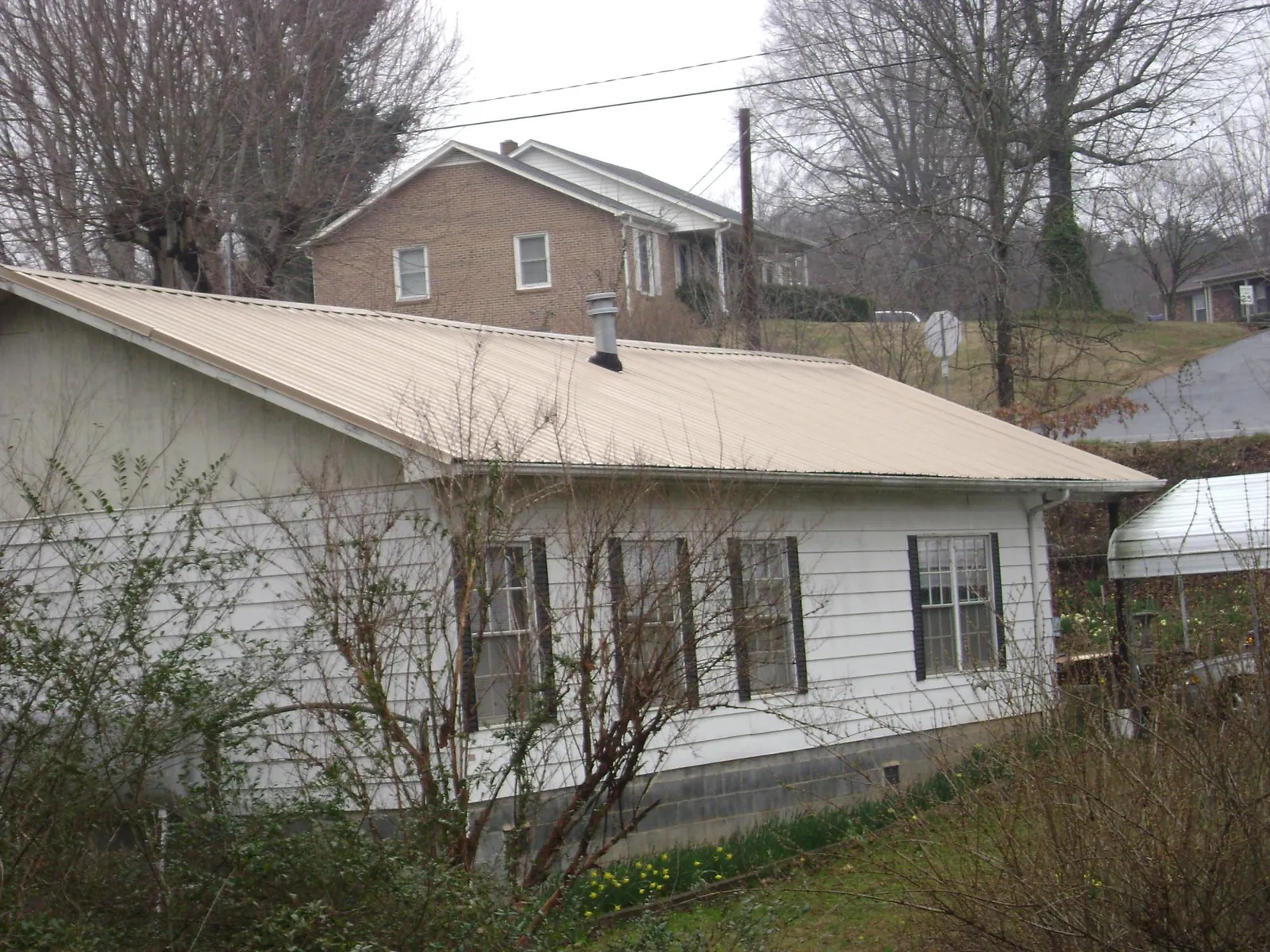 Tan metal roof on a white sided house set into a hillside — Commercial Roofing by Roofing Brothers in Industry